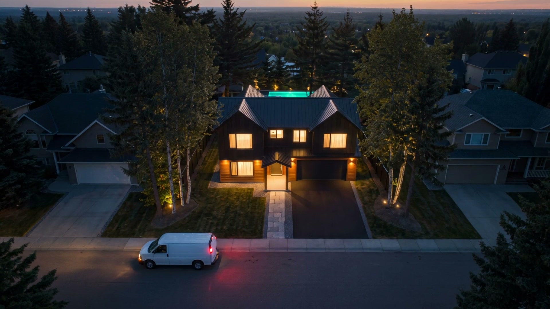 The house from above at nightfall, its windows lit, a work van driving away